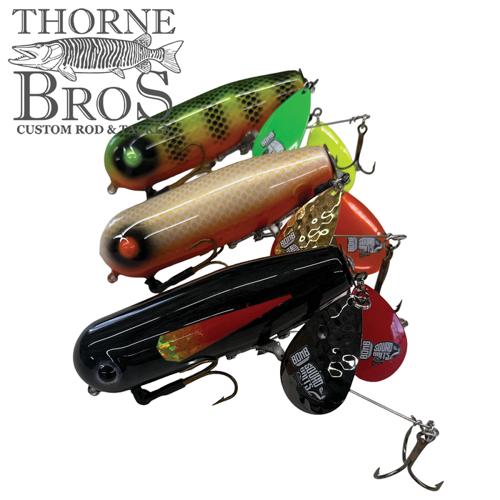 Four detailed fishing lures in various colors including green, orange, yellow, and black, each with multiple hooks and metal flap tails, labeled as Bomb Squad Double Tap Flap Tail.