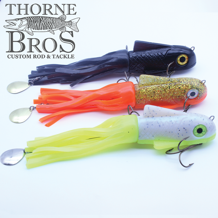 Three Boss Shad Medium Hybrid fishing lures in black, orange with gold glitter, and white with lime green, featuring soft tentacle-like bodies and metal spinner blades attached, arranged on a white background with a Thorne Bros Custom Rod & Tackle logo.