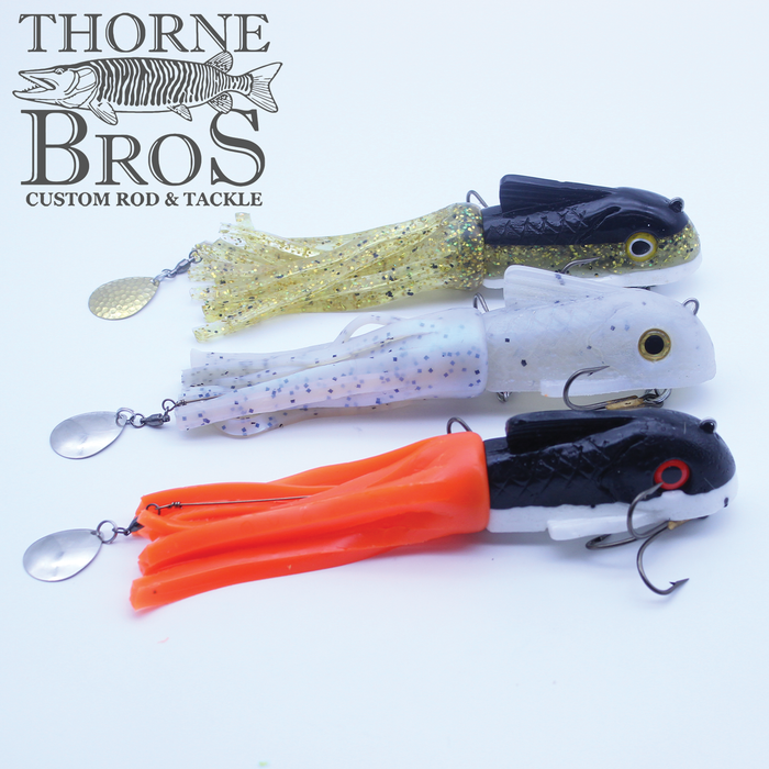 Three Boss Shad Small Hybrid fishing lures in greenish gold, white with blue speckles, and black with orange, each featuring soft skirt tails, realistic eyes, and metal spinner blades.