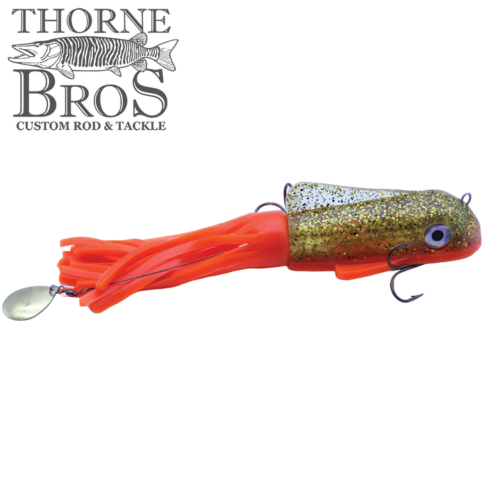 Boss Shad Small Hybrid fishing lure with a gold glitter head, lifelike eyes, bright orange flexible skirt, and treble hooks designed for musky and walleye fishing.