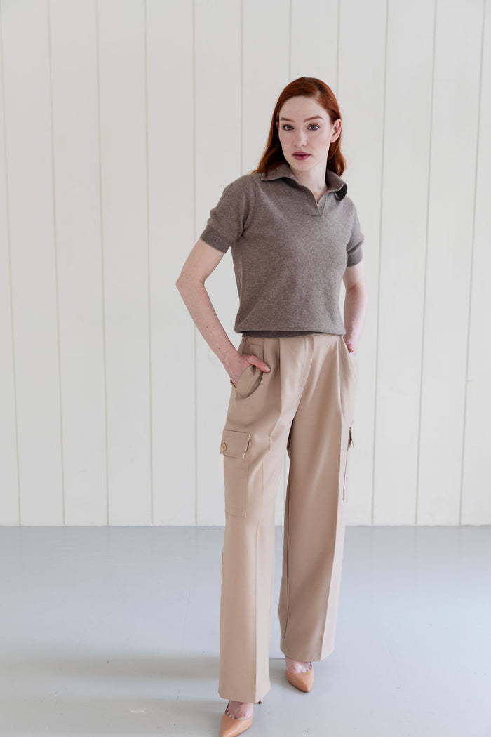 Woman wearing a taupe cashmere polo shirt and beige cargo pants against a white wall.