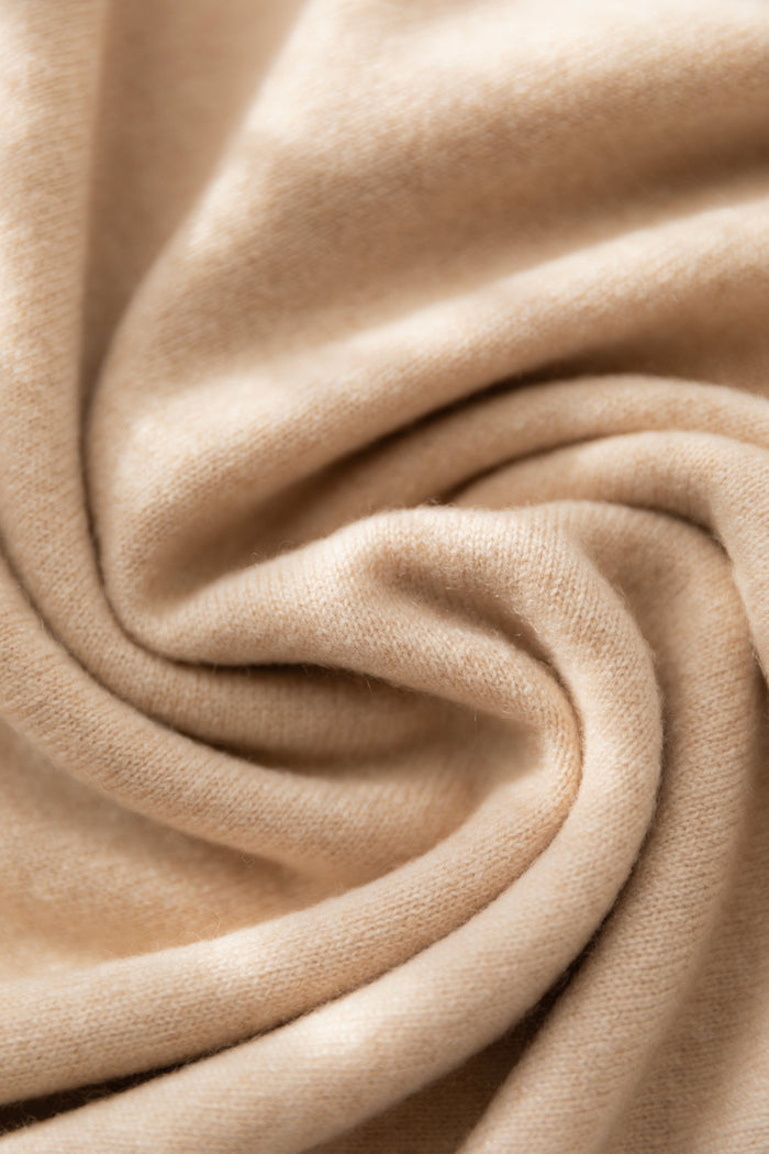 A close-up of a beige cashmere fabric with soft folds and a smooth, slightly lustrous texture.