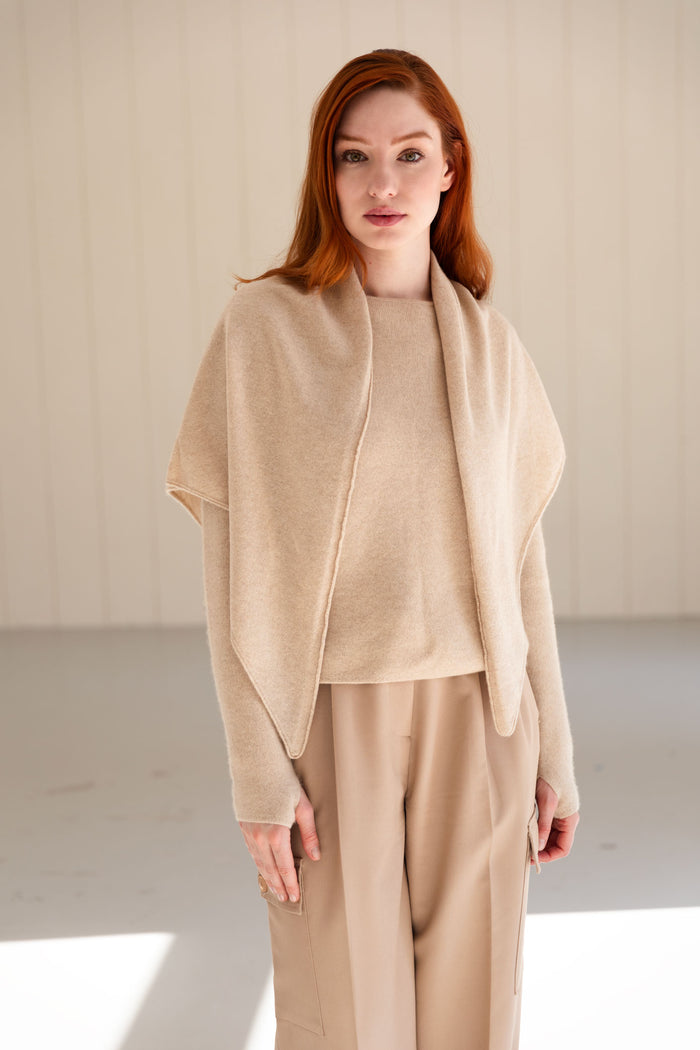 Woman wearing a beige cashmere triangle scarf and pants in a minimalistic setting