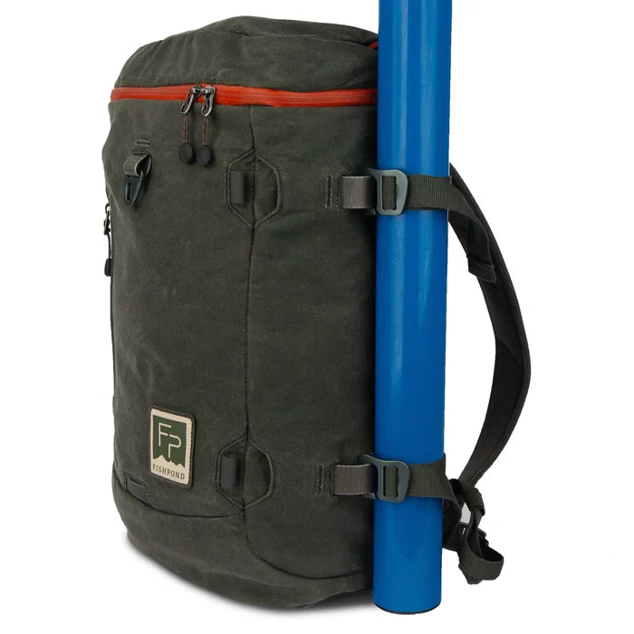 Fishpond River Bank Backpack in dark olive with red zipper, featuring side straps holding a blue fishing rod tube, designed for fishing tackle and gear organization.