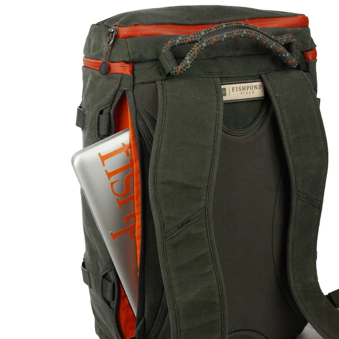 Fishpond River Bank Backpack shown from the back with padded straps, a sturdy handle, and an open side pocket holding a fishing magazine, designed for outdoor fishing activities.