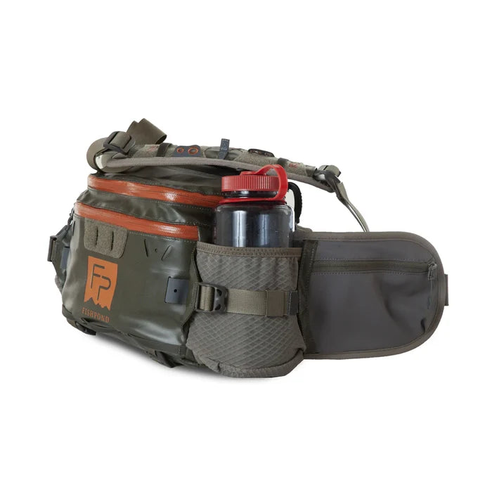 Fishpond Stormshadow Lumbar Pack in olive green and brown with multiple zippered compartments, mesh water bottle holder, padded adjustable strap, and durable outdoor materials for fishing tackle organization.