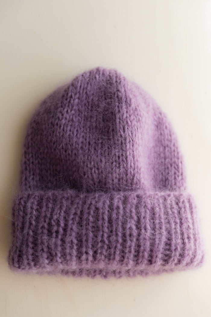 A purple mohair beanie with a ribbed cuff, photographed flat against a plain off-white background.