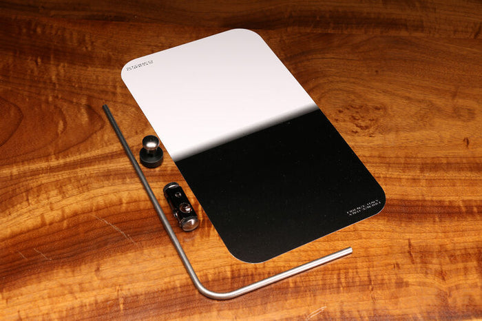 Hareline Profile Plate showing a rectangular, dual-tone black and white tool with accompanying metal hardware pieces and an L-shaped metal rod, placed on a wooden surface.
