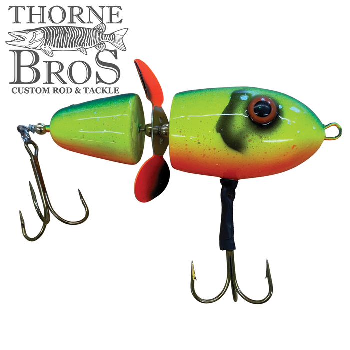 Close-up of a brightly colored fishing lure with green, yellow, and orange shades featuring two treble hooks and a small rear propeller, identified as the Lake-X Hammer.