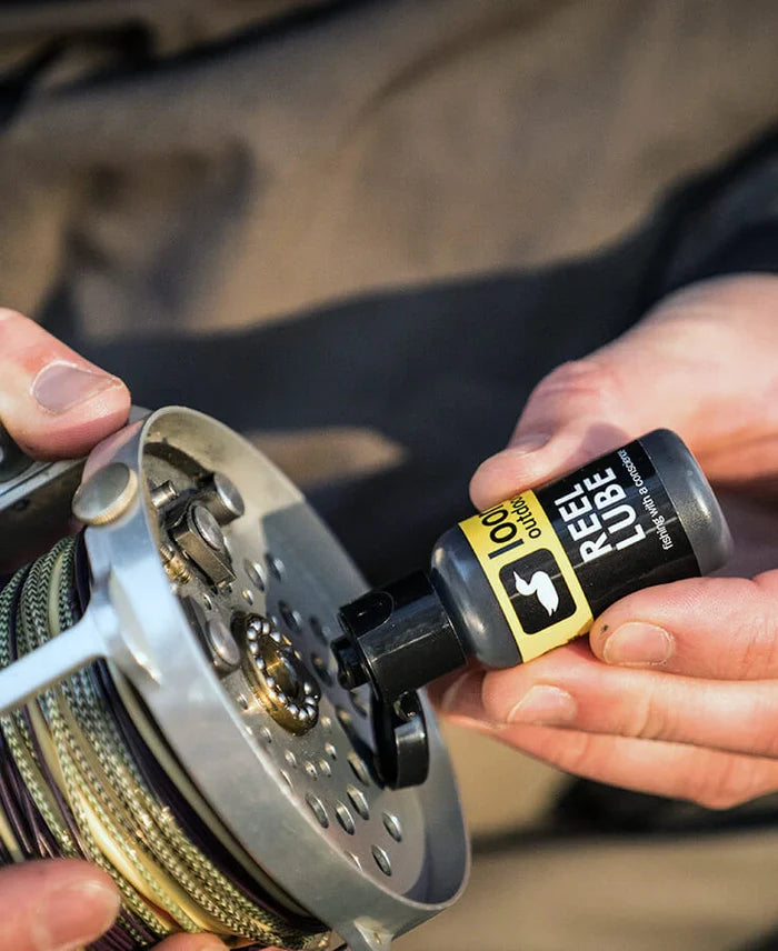 Person applying Loon Outdoors Reel Lube oil to a fishing reel for maintenance, enhancing smooth performance of fishing rods and reels in outdoor use.