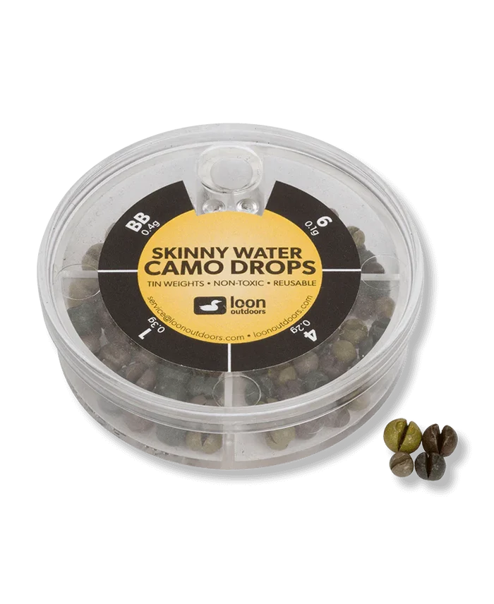 Clear round plastic container holding various sizes of camo-colored tin fishing weights with "Loon Tin Drop Assortments" label on top, alongside four sample weighted drops.