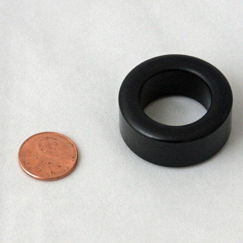 Minn Kota FERRITE, STEWARD P/N: 470085-1 is a small black cylindrical ferrite ring shown next to a penny for size comparison, used in fishing tackle and marine electronics.