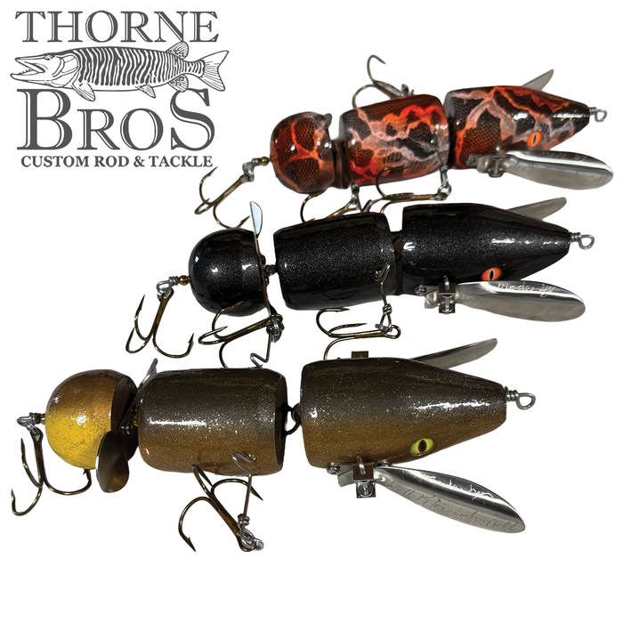 Three segmented fishing lures in yellow, black, and red camo finishes with metal spinner blades and treble hooks, designed as Musky Safari Franken Spitz for fishing tackle.