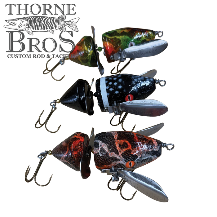 Three Musky Safari Mini Baby Spitzer fishing lures in green, black, and orange patterns with metal spinner blades and treble hooks, displayed next to Thorne Bros logo.