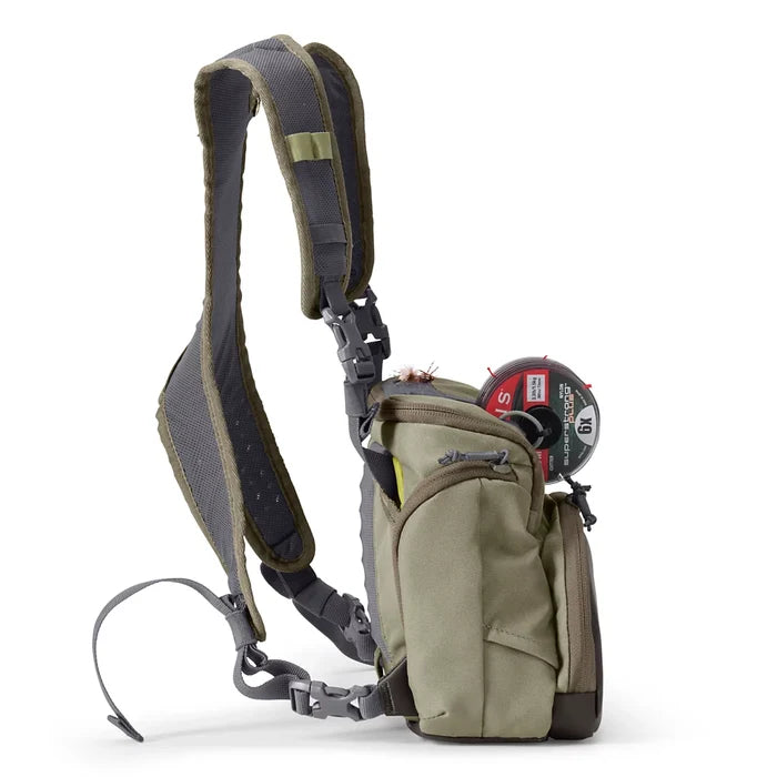 Orvis Chest Pack in olive green with multiple zippered compartments, adjustable padded shoulder strap, and attached fishing fly gear, designed for convenient carrying of fishing tackle.