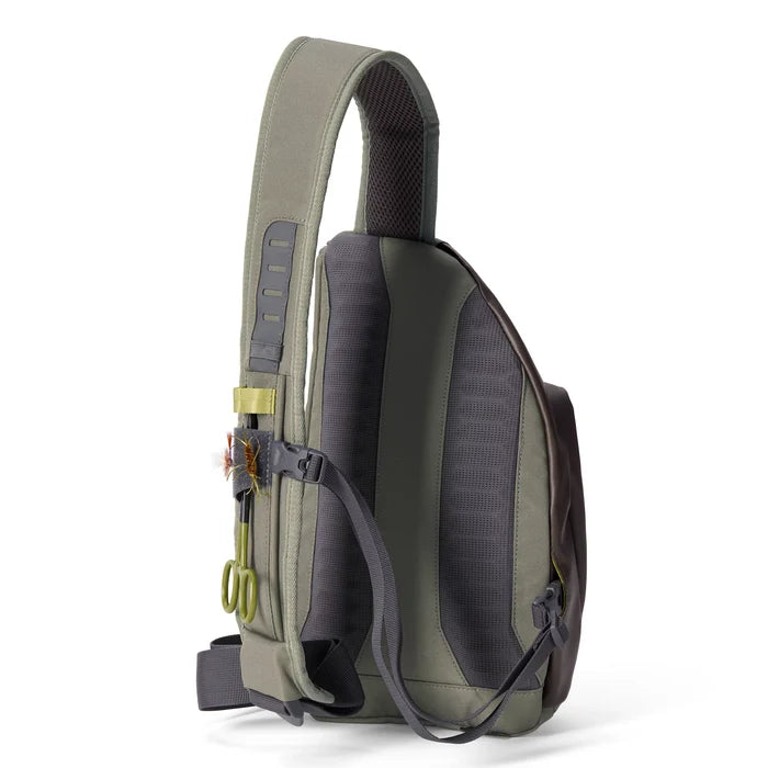 Orvis Mini Sling Pack in muted green and gray tones with padded back panel, adjustable strap, and attachments for fishing tools, designed for comfortable outdoor use.