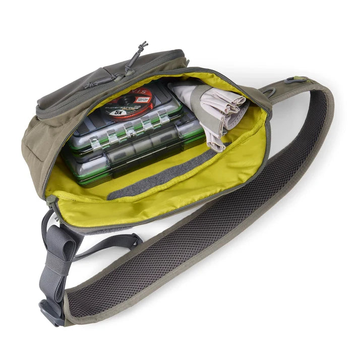 Orvis Mini Sling Pack in olive green with padded, breathable shoulder strap, open to show organized fishing tackle boxes and folded fabric inside.