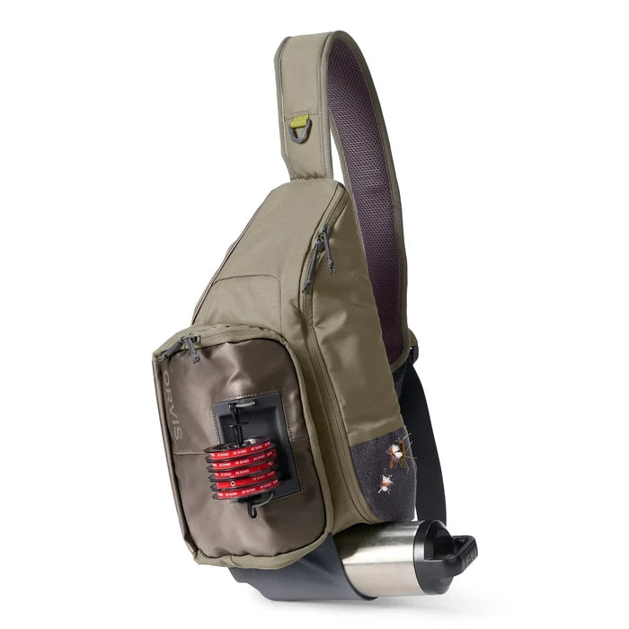 Orvis Sling Pack in olive and brown tones with multiple zippered compartments, featuring a front fishing line spool holder and a side mesh pocket, designed for convenient fishing tackle storage.