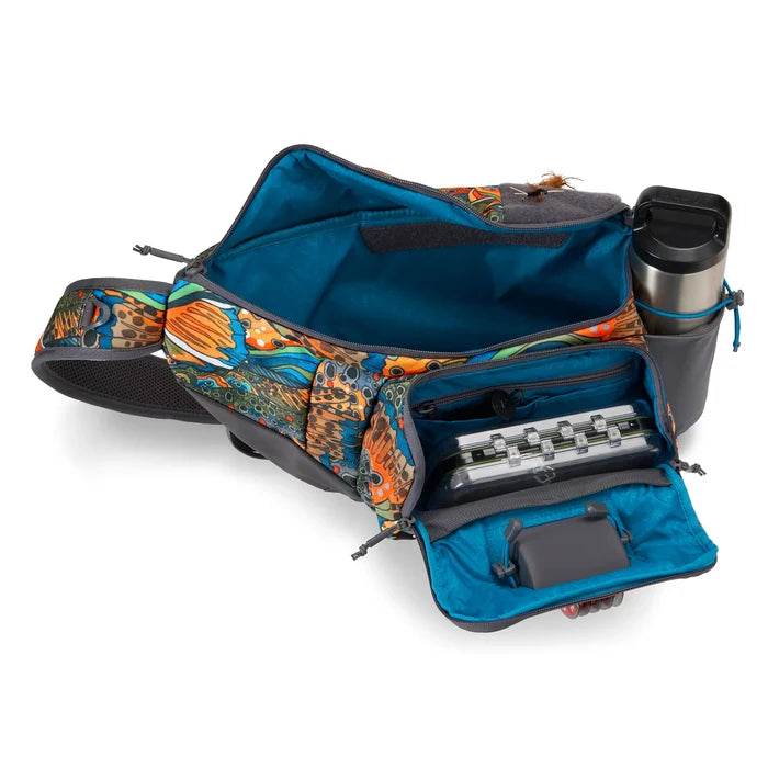 Orvis Sling Pack shown open with multiple zippered compartments revealing organized fishing tackle boxes and a side pocket holding a stainless steel water bottle, featuring a colorful aquatic-themed pattern.