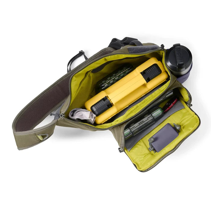 Orvis Sling Pack shown open with organized compartments holding a yellow tackle box, fishing tools, and a water bottle, designed for convenient fishing tackle storage.
