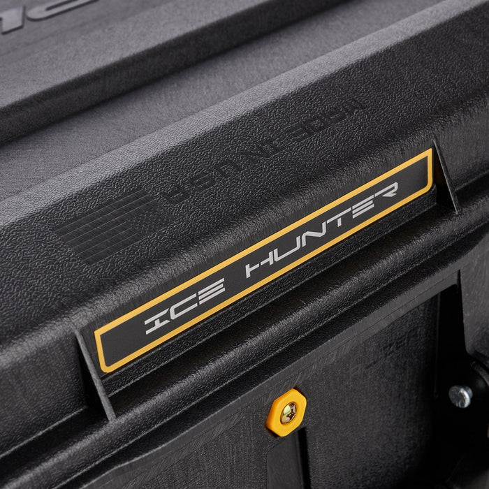 Close-up of the textured black Plano Ice Hunter 44" Ice Combo Case showing a yellow and black label with "ICE HUNTER" text and a yellow screw detail on the rugged exterior.