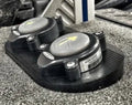 Close-up of the black Precision Sonar Stomp Station for Power Pole and Minn Kota Raptor - Double PN:SWS-DBLE mounted on a textured gray surface, showing two circular stomp pads with yellow arrows.