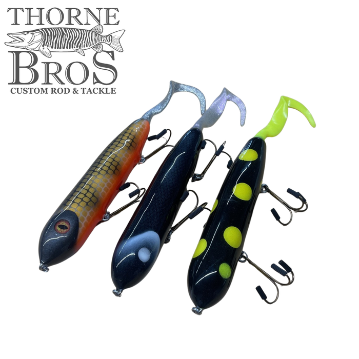 Three Holmgren Serpent Musky Top Water fishing lures in different colors, featuring curved tails and multiple treble hooks, displayed on a white background with Thorne Bros logo.