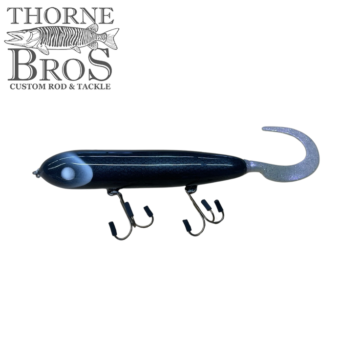 Holmgren Serpent Musky Top Water fishing lure in dark blue with a curled tail and two sets of sharp treble hooks, designed for top water musky fishing.
