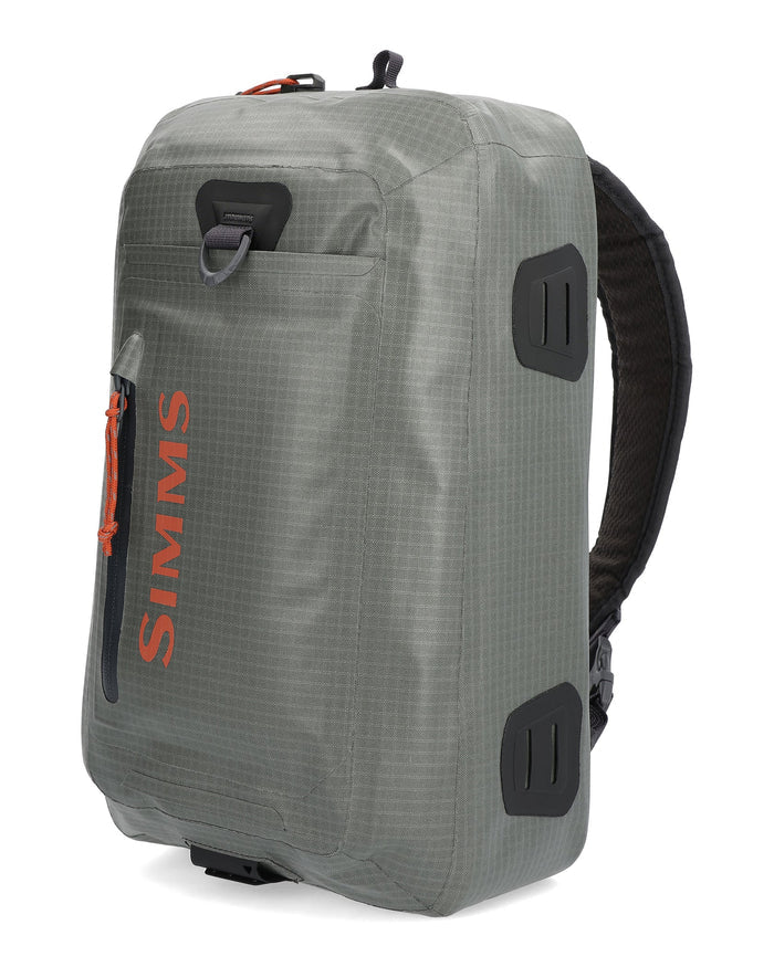 Simms Dry Creek Z Sling Pack in gray with orange zipper pull and logo, featuring durable fabric, multiple compartments, and padded adjustable sling strap for fishing tackle storage.