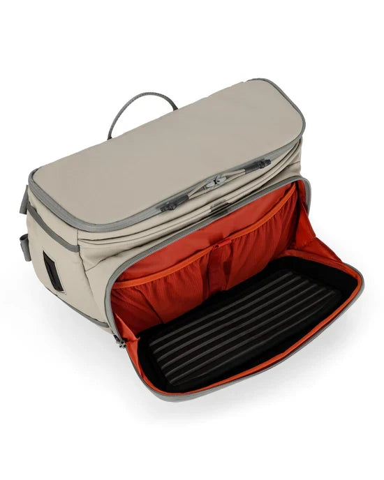 Simms Headwaters Sling Pack in beige with a zippered main compartment open to reveal an orange interior and multiple organizer pockets, designed for fishing tackle storage.