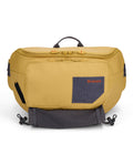 Simms Tributary Hip Pack in mustard yellow with multiple zippered compartments, a front felt patch with embroidered logo, and adjustable straps for secure, comfortable carry.