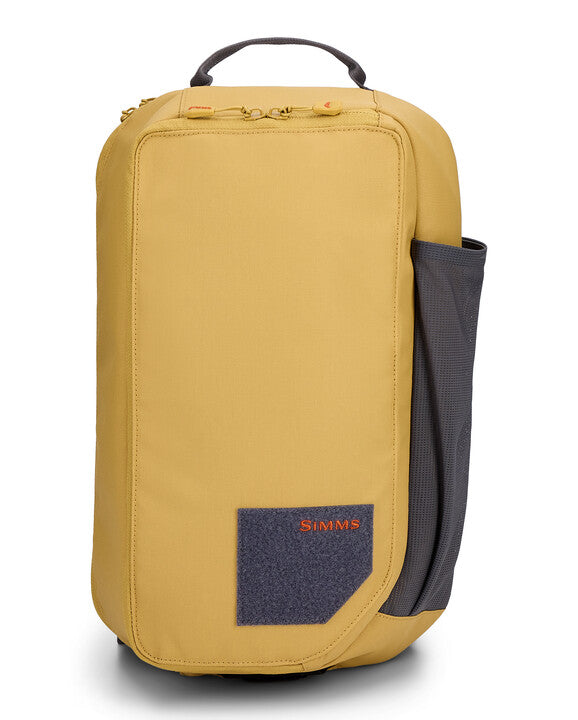 Simms Tributary Sling Pack in mustard yellow with a black mesh side pocket, top handle, and front patch featuring the Simms logo, designed for organizing fishing tackle.