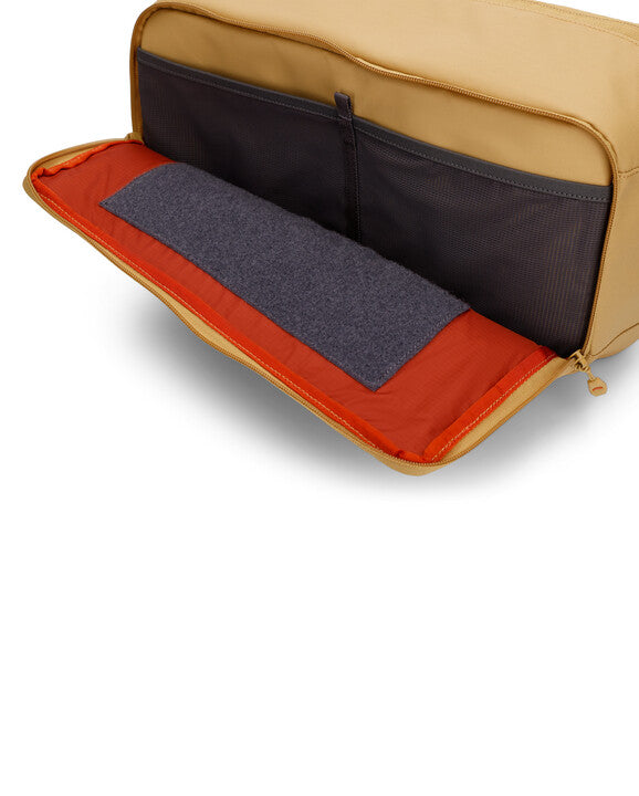 Interior view of an open tan Simms Tributary Sling Pack showing an orange interior with black mesh pockets and a gray padded section for organized fishing tackle storage.