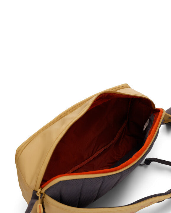 Simms Tributary Sling Pack in tan with open main compartment showing spacious red interior lining and padded back panel designed for carrying fishing tackle and accessories.