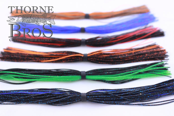 Close-up of multiple Starflash Musky Skirt 7'' Strand fishing lures in various colors, arranged horizontally, designed for use in musky fishing tackle.
