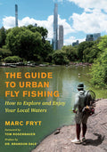 Cover of "The Guide To Urban Fly Fishing" showing an angler standing on a rocky shore casting a fly fishing rod into a calm urban waterway with city skyscrapers and green trees in the background.