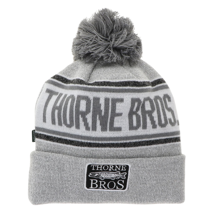 Thorne Bros Cuff Pom Beanie in gray tones featuring a large pom-pom on top, bold "THORNE BROS" knit lettering, and a cuff label with fishing lure graphic for cold weather wear.