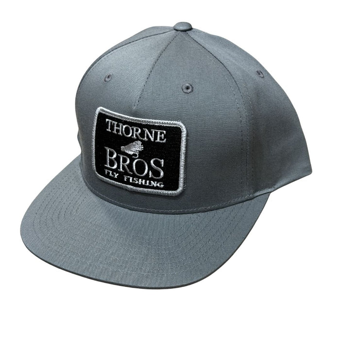 Gray baseball cap with a black and white embroidered patch reading "Thorne Bros Fly Fishing," featuring a structured crown and flat brim, called Thorne Bros Fly Fishing Logo Richardson 255 Flint Grey.