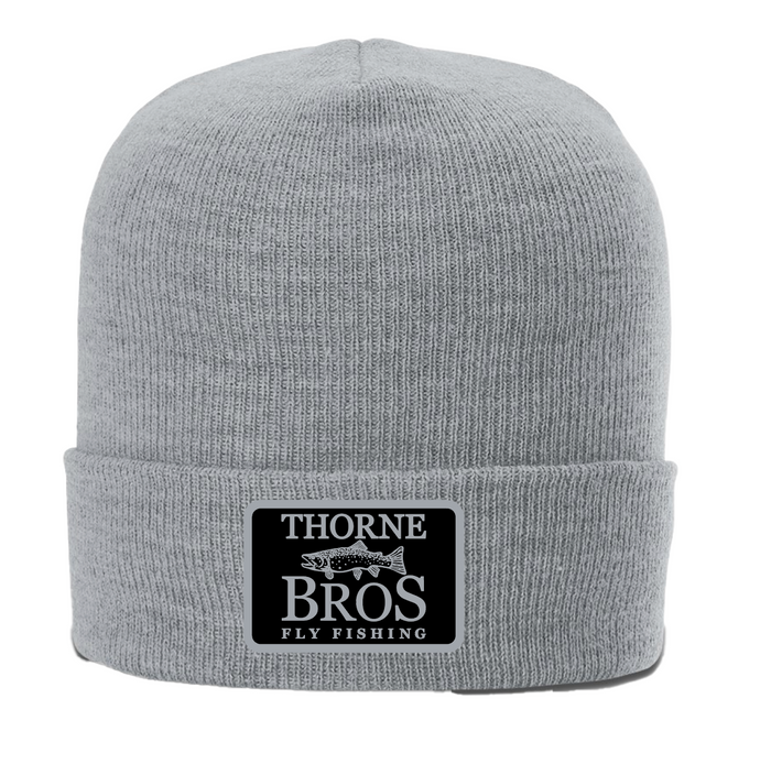 Light gray knit beanie with a folded cuff featuring a black patch with white text and a trout graphic, labeled Thorne Bros. Fly Fishing, Thorne Bros. Fly Fishing Trout Logo Cuff Beanie.