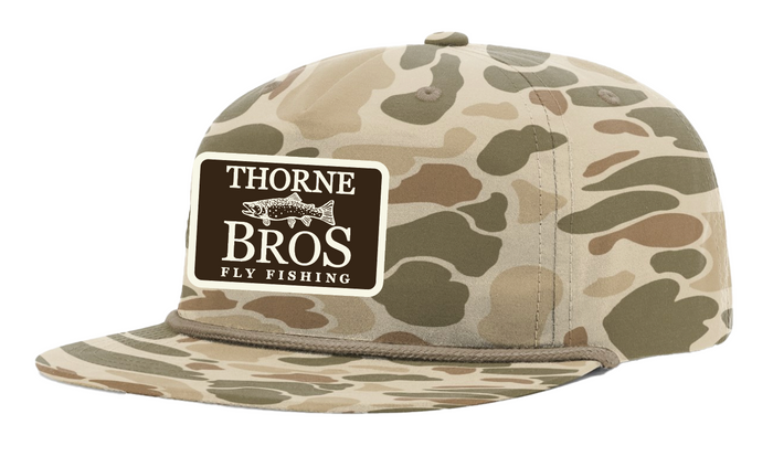 Thorne Bros Fly Fishing Trout Logo Richardson Umpqua 256P Light Brown camo-patterned hat with adjustable back and stitched logo patch on front, designed for outdoor fishing enthusiasts.