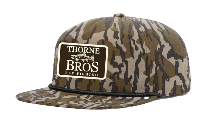 Thorne Bros Fly Fishing Trout Logo Richardson Umpqua 256P MO Bottomland camo patterned hat with embroidered logo patch and black cord detail on the brim.