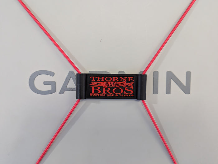 Thorne Bros Graph Cover Strap in black with red logo, designed to secure fishing rods and tackle, shown holding bright red cords against a light background.