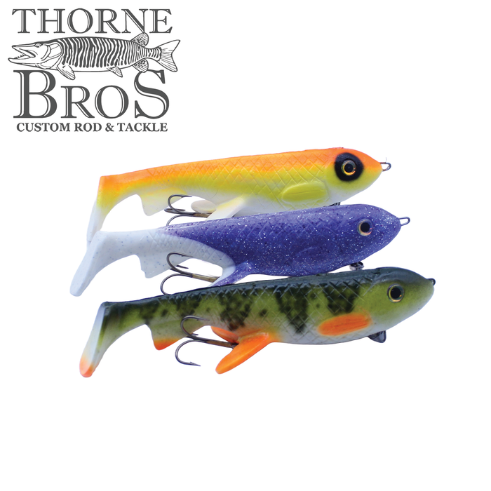 Three Trophy Systems Bait Co. 10" Osprey fishing lures in yellow-orange, purple, and green with orange accents, each featuring detailed eyes and treble hooks for fishing tackle.