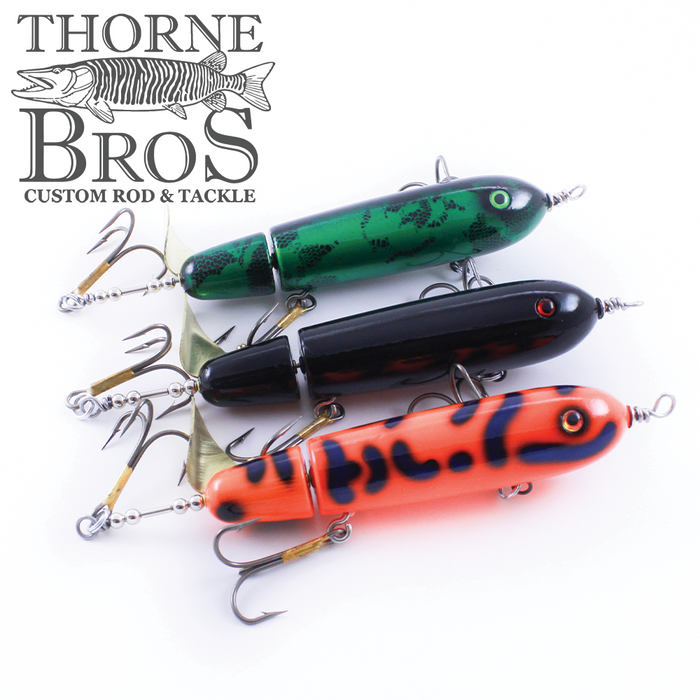 Three fishing lures in green, black, and orange with black spots, each featuring multiple metal treble hooks, displayed with the Ty Sennett Pacemaker - Wood logo for fishing tackle.