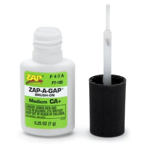 Small white bottle of Zap Brush On adhesive with a green and yellow label next to its black brush applicator cap.